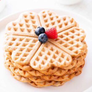 Vegane Waffeln ohne Zucker auf einem weißen Teller, dekoriert mit einer Himbeere und Heidelbeeren.