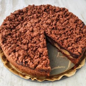Ein runder veganer Schokoladenkuchen mit Schokostreuseln, einer Schokopuddingschicht und Birnenstücken, bei dem bereits ein Stück herausgeschnitten wurde.