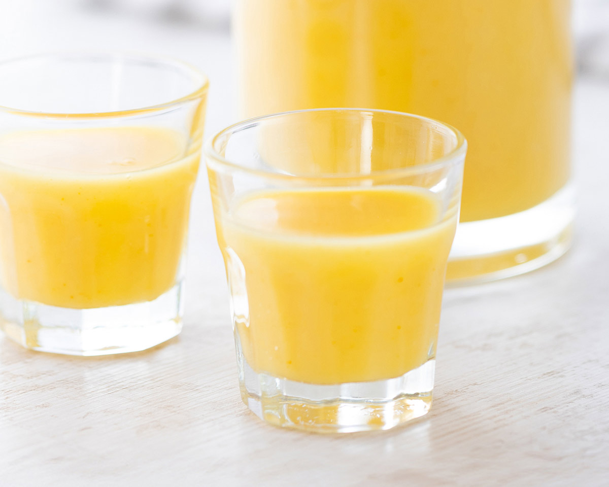 Zwei Likörgläser mit veganem Eierlikör, im Hintergrund eine Flasche mit veganem Eierlikör.