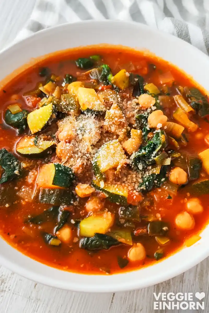 Teller mit veganem Eintopf aus Kichererbsen, Zucchini und Spinat auf hellem Untergrund