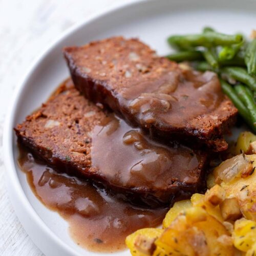 Vegane Scheiben Hackbraten aus Kidneybohnen und Linsen mit Soße, grünen Bohnen und Bratkartoffeln, serviert auf einem weißen Teller.