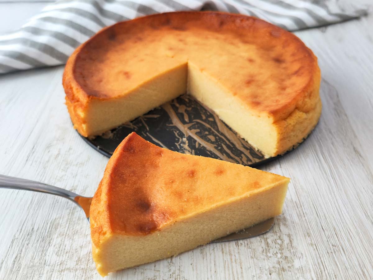 Ein veganer Käsekuchen ohne Boden mit leicht gebräunter Oberfläche, ein Stück liegt davor auf einem Tortenheber.