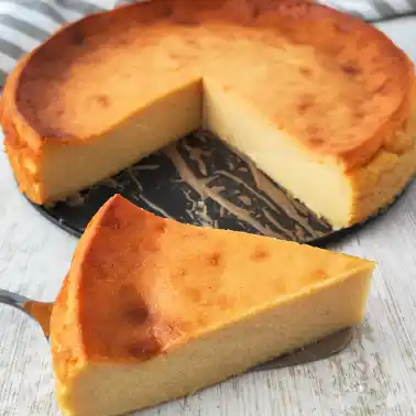 Ein veganer Käsekuchen ohne Boden mit leicht gebräunter Oberfläche, ein Stück liegt davor auf einem Tortenheber.