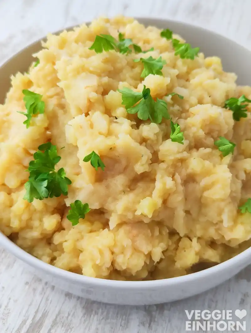 Weiße Servierschüssel mit veganem Kartoffel Sellerie Stampf, bestreut mit frischer Petersilie.