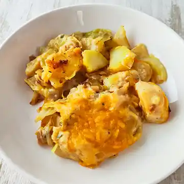 Eine Portion veganer Kartoffel-Spitzkohl-Auflauf mit geschmolzenem veganem Käse auf einem weißen Teller serviert.
