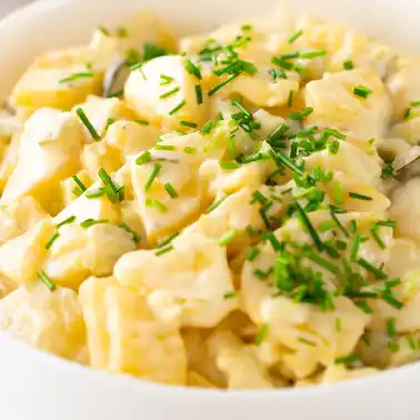 Veganer Kartoffelsalat mit Mayo, garniert mit frisch geschnittenem Schnittlauch, serviert in einer weißen Schüssel.