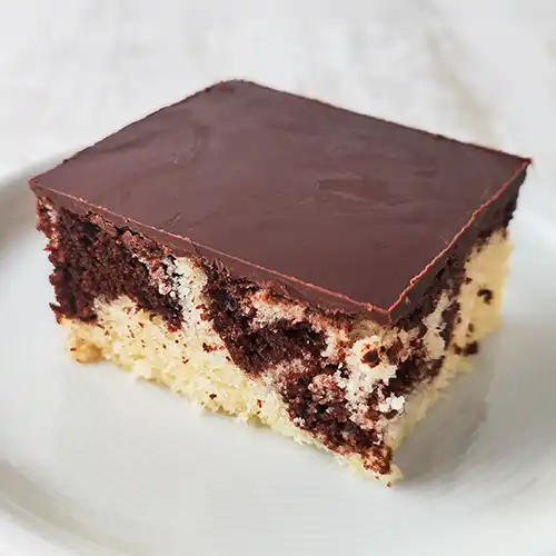 Ein Stück veganer Marmorkuchen vom Blech mit Schokoglasur liegt auf einem weißen Teller.