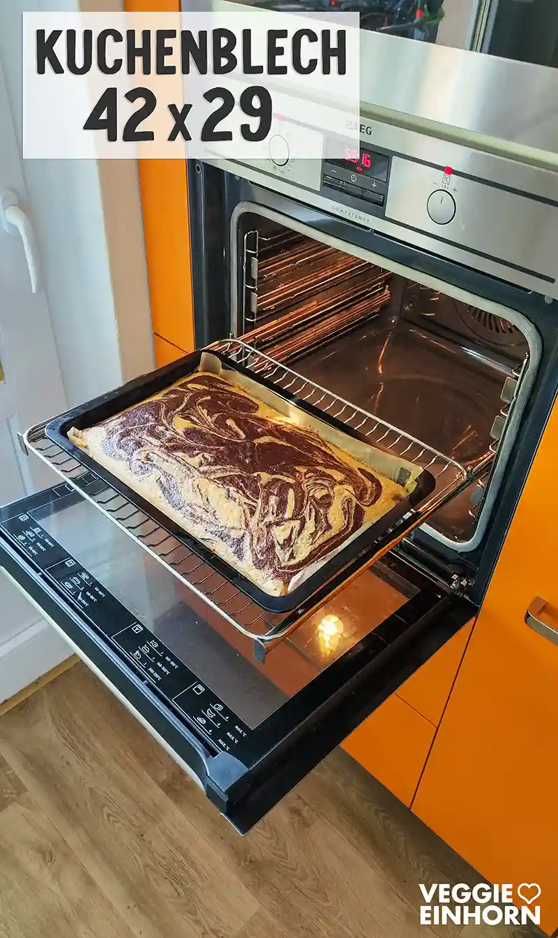 Frisch gebackener veganer Marmorblechkuchen im Backblech mit marmorierter Teigstruktur vor einem geöffneten Backofen.