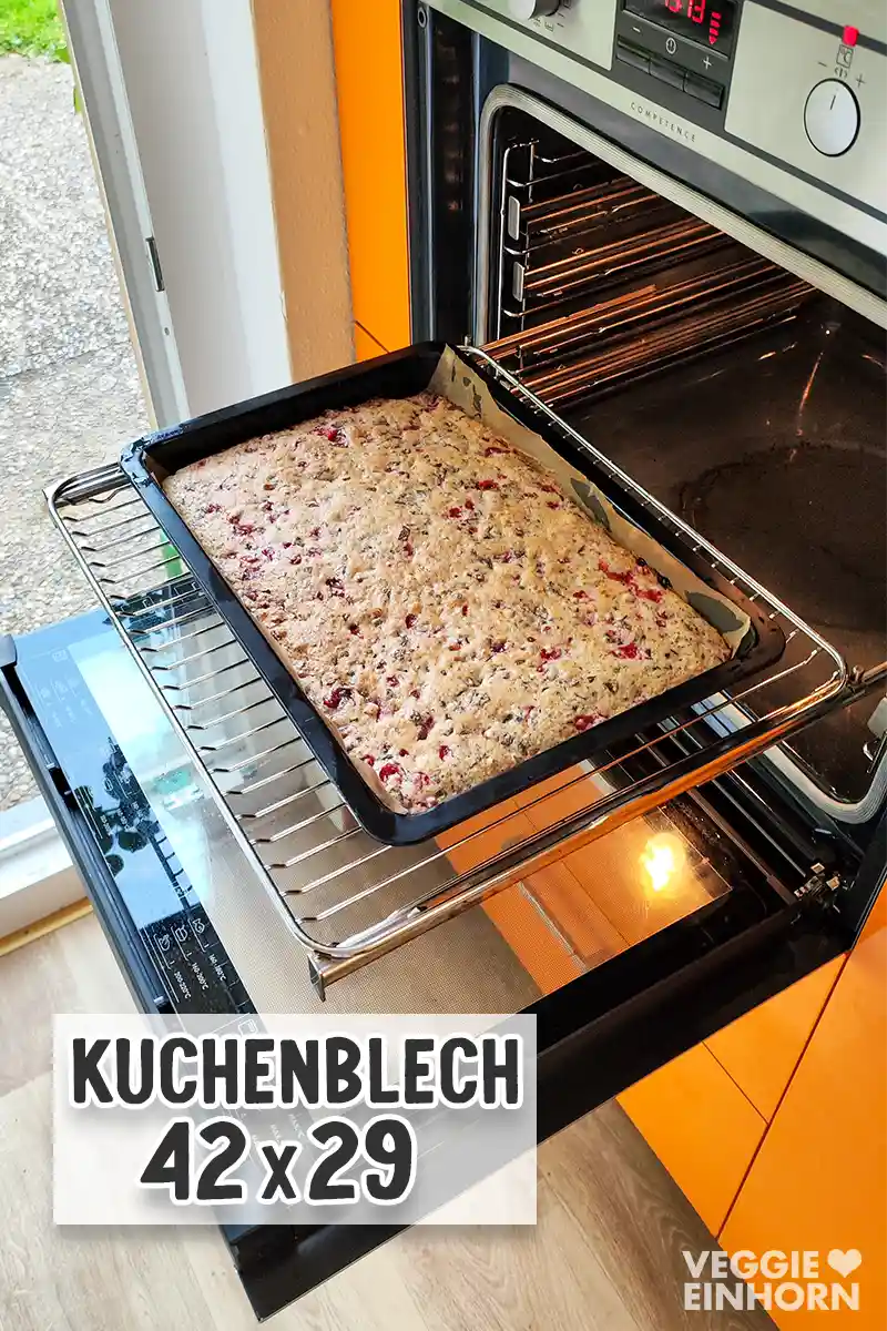 Ein frisch gebackener veganer Johannisbeerkuchen vor dem geöffneten Backofen. Die Aufschrift auf dem Bild zeigt die Blechgröße 42 x 29 cm.