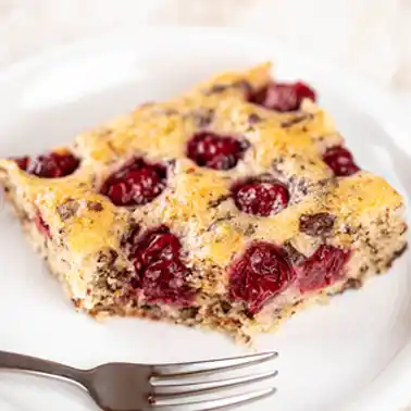 Veganer Nusskuchen vom Blech mit saftigen Kirschen, serviert auf einem weißen Teller mit Kuchengabel.