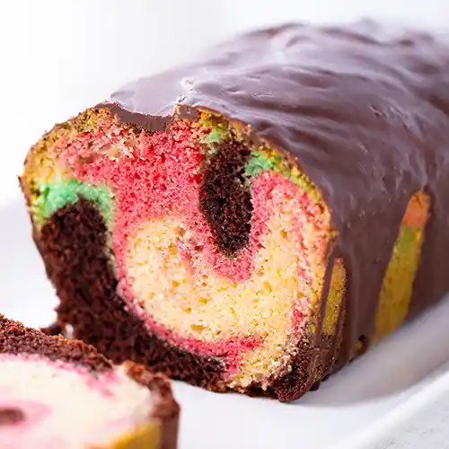 Anschnitt eines veganen Papageienkuchens aus der Kastenform mit kräftig gemusterten Farben und Schokoglasur.