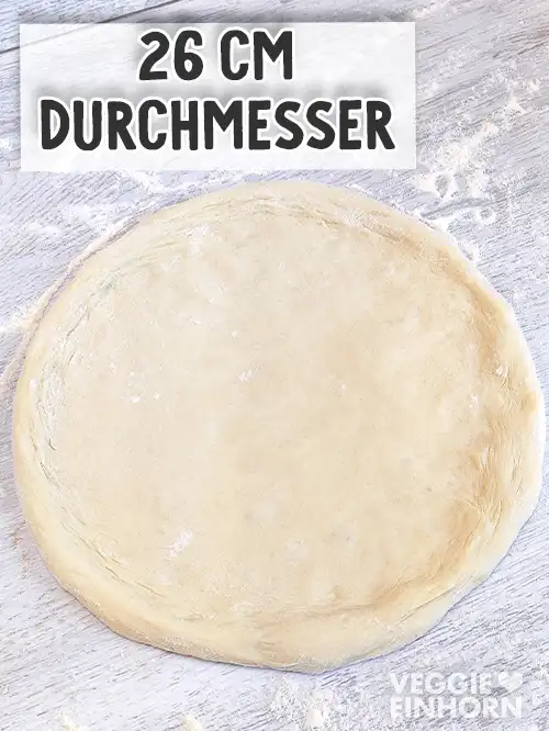 Ein runder Pizzaboden liegt auf einer bemehlten Arbeitsfläche und hat einen Durchmesser von 26 cm.