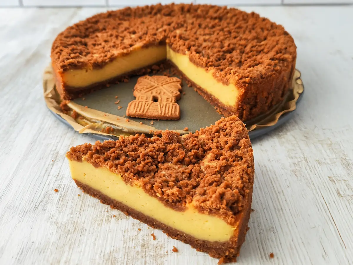 Veganer Spekulatius Käsekuchen auf einem Springformboden, ein Stück ist heraus geschnitten und liegt davor.