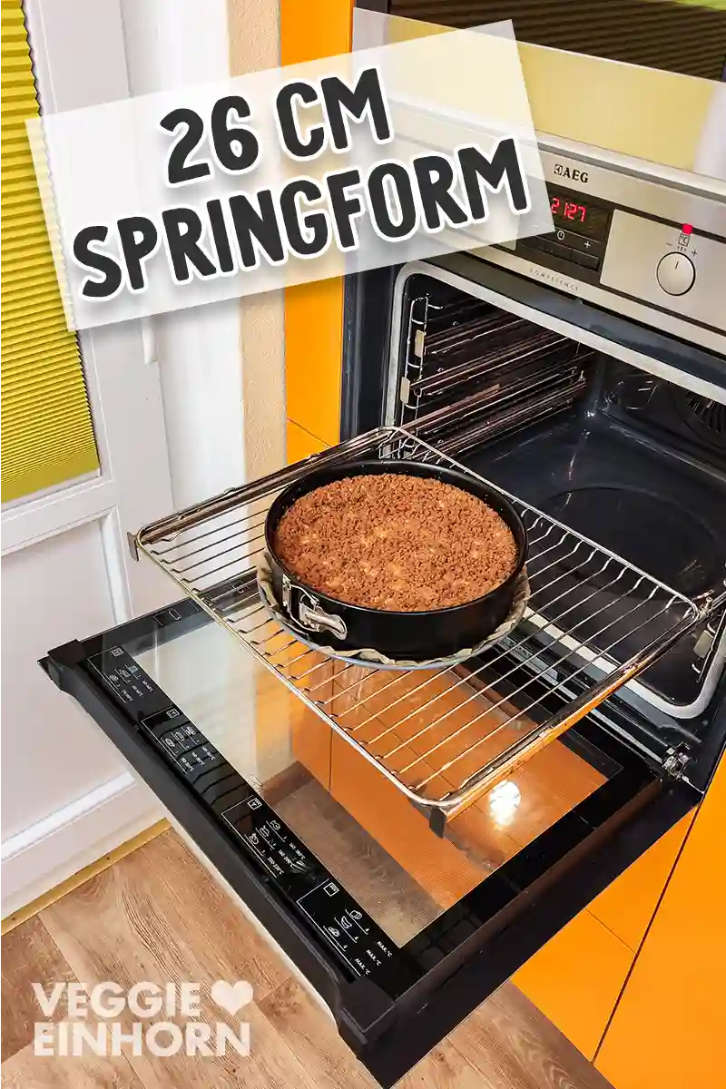Eine 26 cm Springform mit veganem Spekulatius Käsekuchen steht auf einem Backofengitter im Ofen, der Kuchen ist goldbraun gebacken.