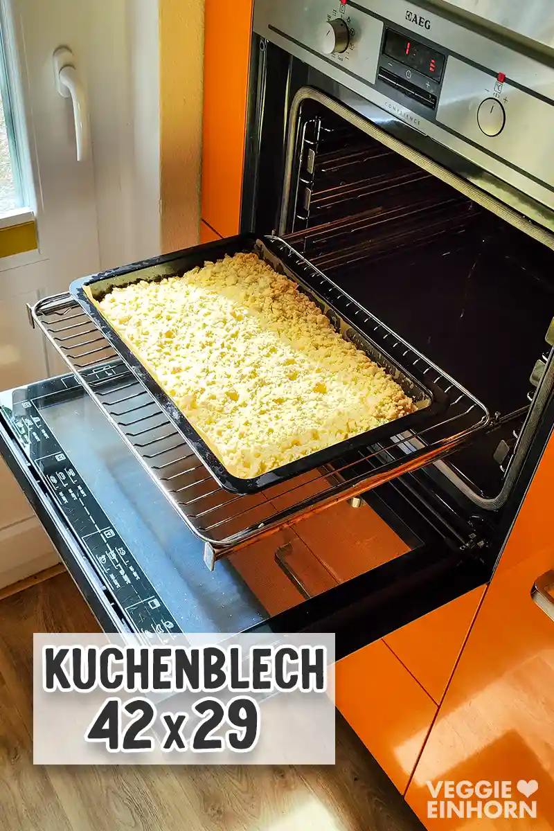 Ein Kuchenblech mit veganem Streuselkuchen steht auf einem Backofenrost in einem geöffneten Backofen.