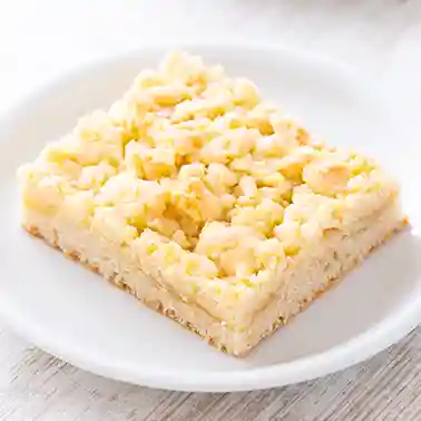 Ein Stück veganer Blechkuchen mit Streuseln liegt auf einem weißen Teller.