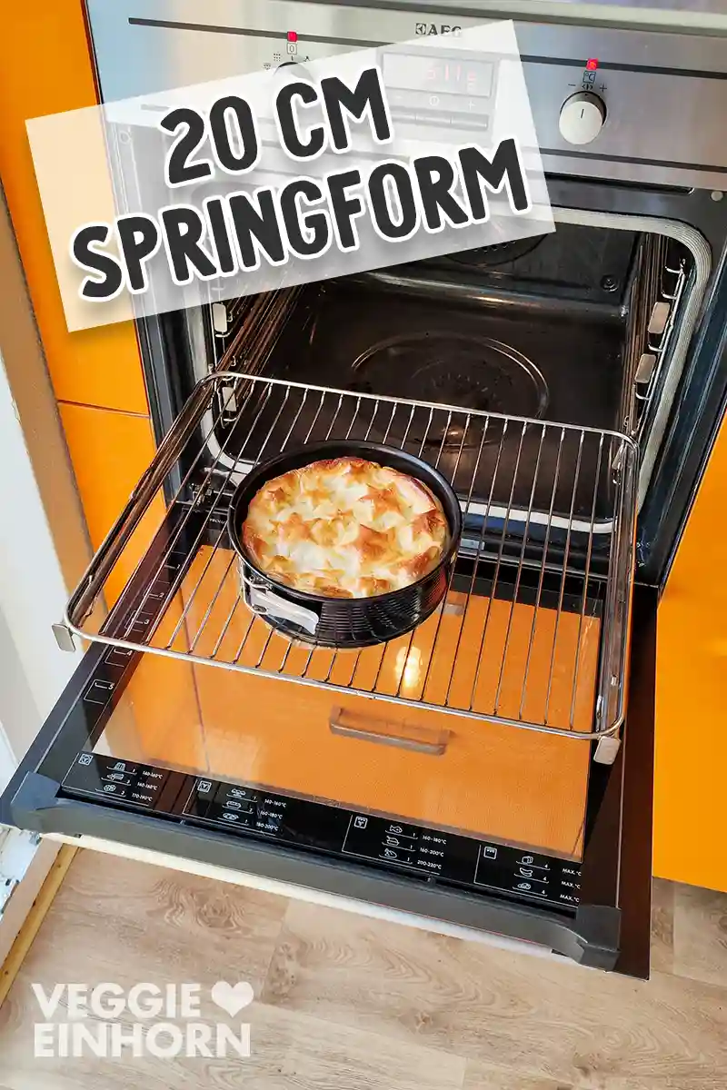 Eine runde 20-Zentimeter-Springform mit einem goldbraunen veganen Blätterteigbraten steht auf einem Backofenrost im geöffneten Ofen.