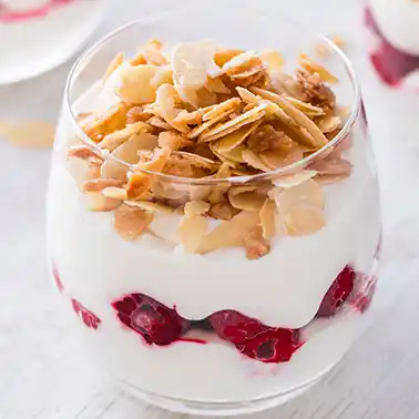 Glas mit veganem Schichtdessert mit Dessertcreme, TK Himbeeren und karamellisierten Mandelblättchen.