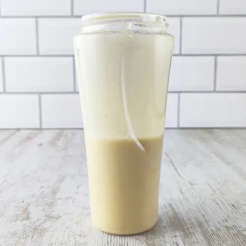 Veganes Hummus-Dressing im hohen Mixerbehälter auf hellem Holztisch.