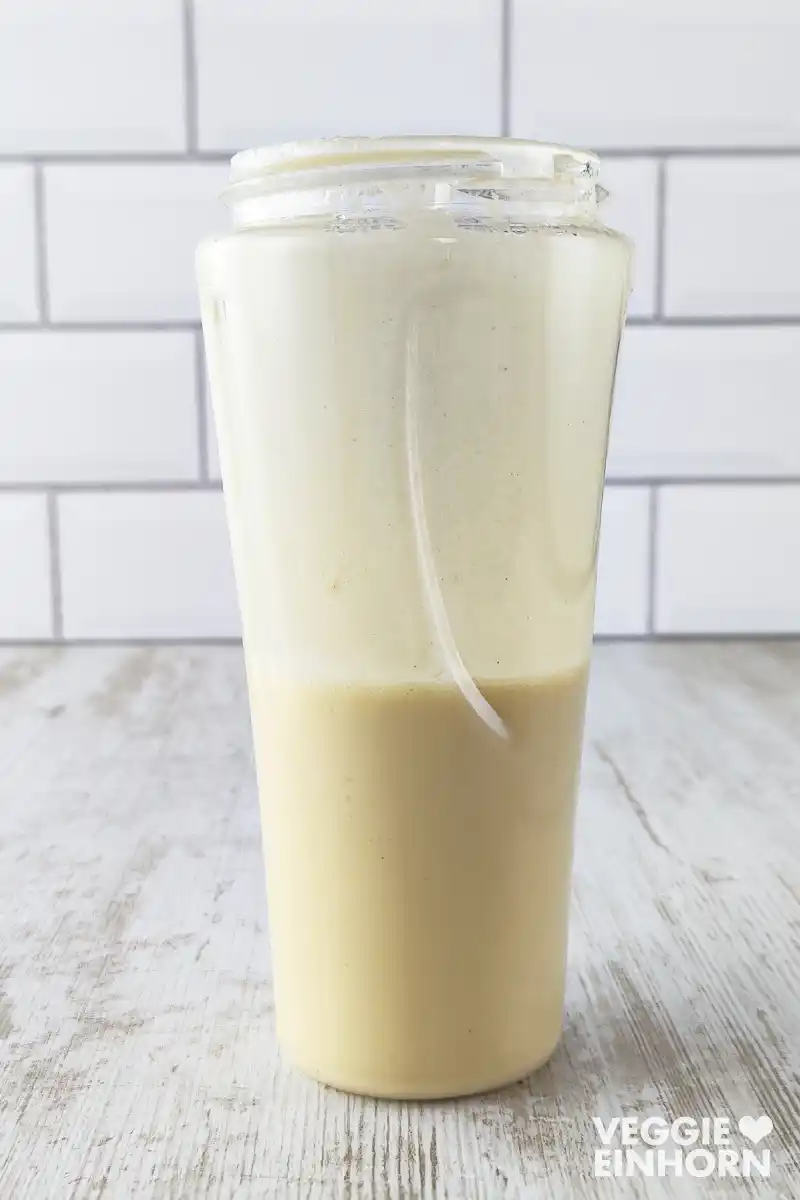 Hummus-Dressing in einem Mixbecher vor weißer Fliesenwand.