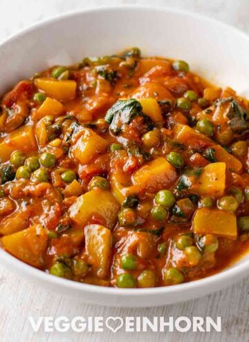 Teller mit veganem Kartoffelcurry mit Spinat und Erbsen