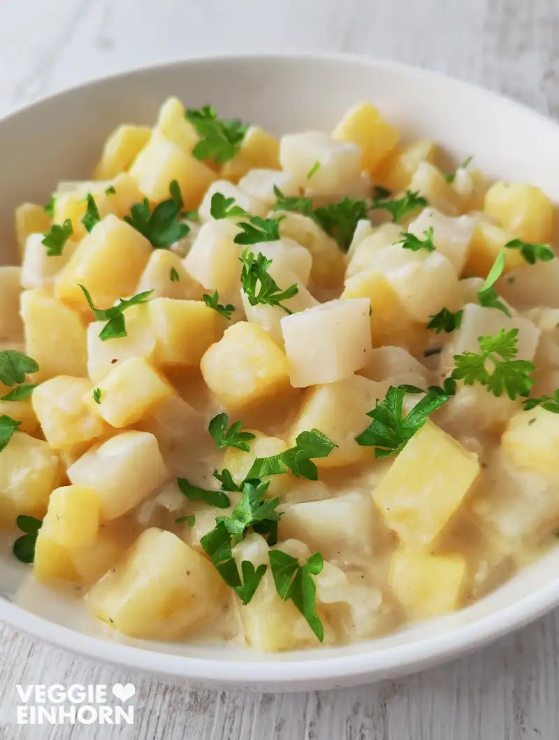 Veganes Kohlrabi-Kartoffel-Gemüse in heller Soße auf einem Teller, garniert mit frischer Petersilie.