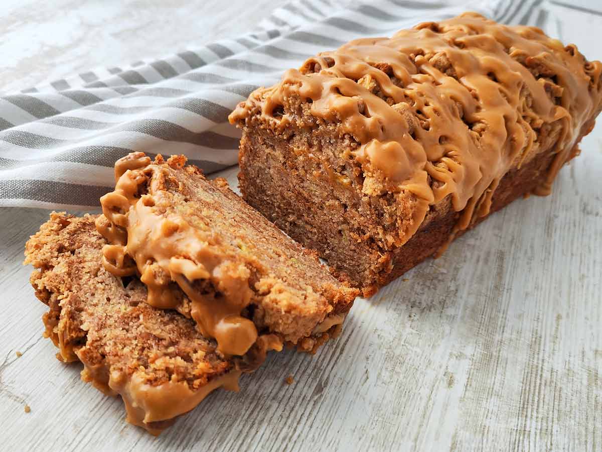 Anschnitt eines veganen Spekulatius Bananenbrots mit Karamellglasur auf einem hellen Holztisch, daneben ein gestreiftes Tuch.