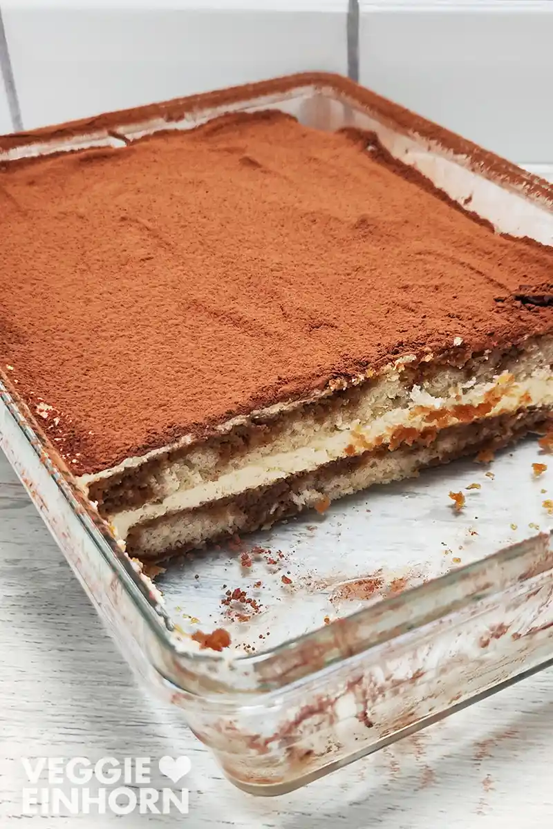 Ein veganes Tiramisu in einer Glasform zeigt mehrere Schichten aus Biskuit, Creme und Kakaopulver.