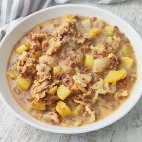 Ein Teller mit veganem Wirsingeintopf mit Kartoffeln und veganem Hack steht auf einem hellen Holztisch.