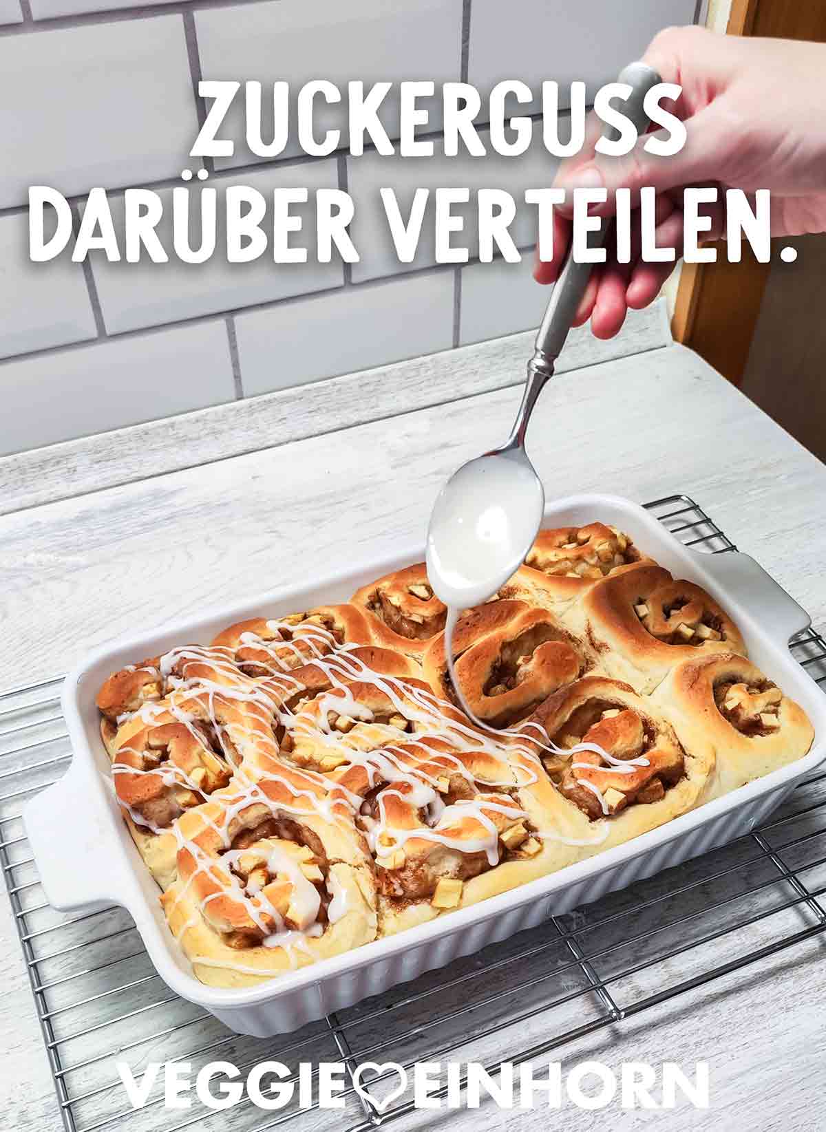 Mit einem Löffel wird Zuckerguss über gebackene Apfel-Zimt-Schnecken verteilt.
