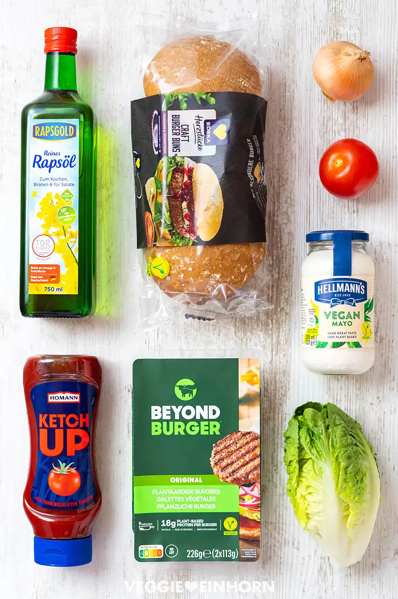 Zutaten für einen veganen Burger: Rapsöl, Burgerbrötchen, Tomate, Zwiebel, vegane Mayonnaise, Ketchup, Beyond Burger Patties und Romana-Salat.